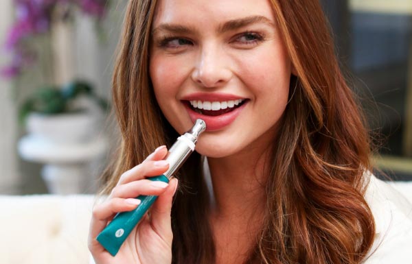 A smiling woman using the Lip Plumping Serum on her lips.